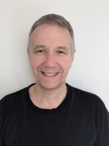 Man with short hair smiling and wearing a black tshirt.