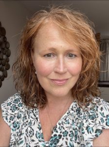 Lady with read hair, smiling and wearing a flowery dress.