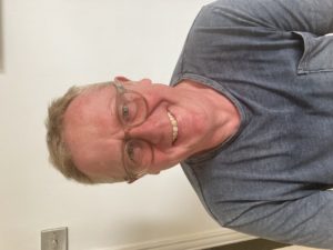 Man with shorrt hair, smiling wearing glasses and a grey tshirt