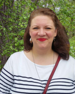 Lady with long brown hair and red lipstick, wearing a black and white striped top.