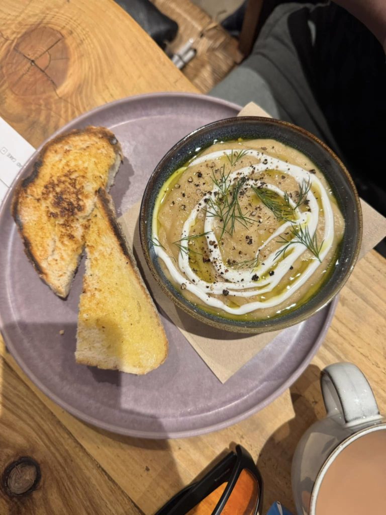 The image shows some of the food which was available at the café. It is a potato soup with goat labneh, which is a form of yoghurt made from goats cheese. The soup was served with a slice of toasted bread.