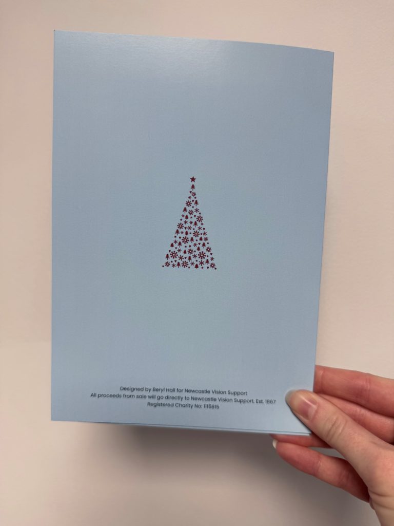 The back of the Christmas Card. The card is blue and there is a small red tree in the centre. The tree is made up of love hearts, trees and snowflakes.
The text at the bottom of the card reads - Designed by Beryl Hall for Newcastle Vision Support. All proceeds from sale will go directly to Newcastle Vision Support. Est. 1867. Registered Charity No: 1115815.